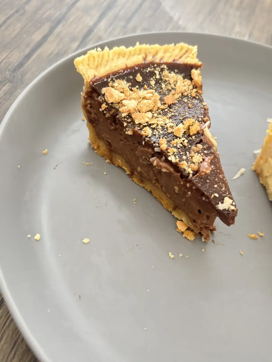 Satu potong Kue Lontar cokelat lumer dengan remahan Regal di atas piring abu-abu