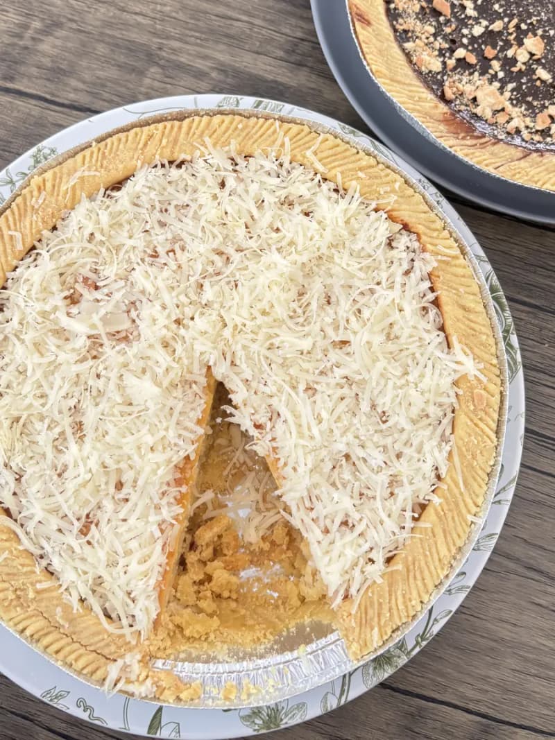 Loyang Kue Lontar keju yang sudah dipotong, lapisan custard terlihat di bawah parutan keju