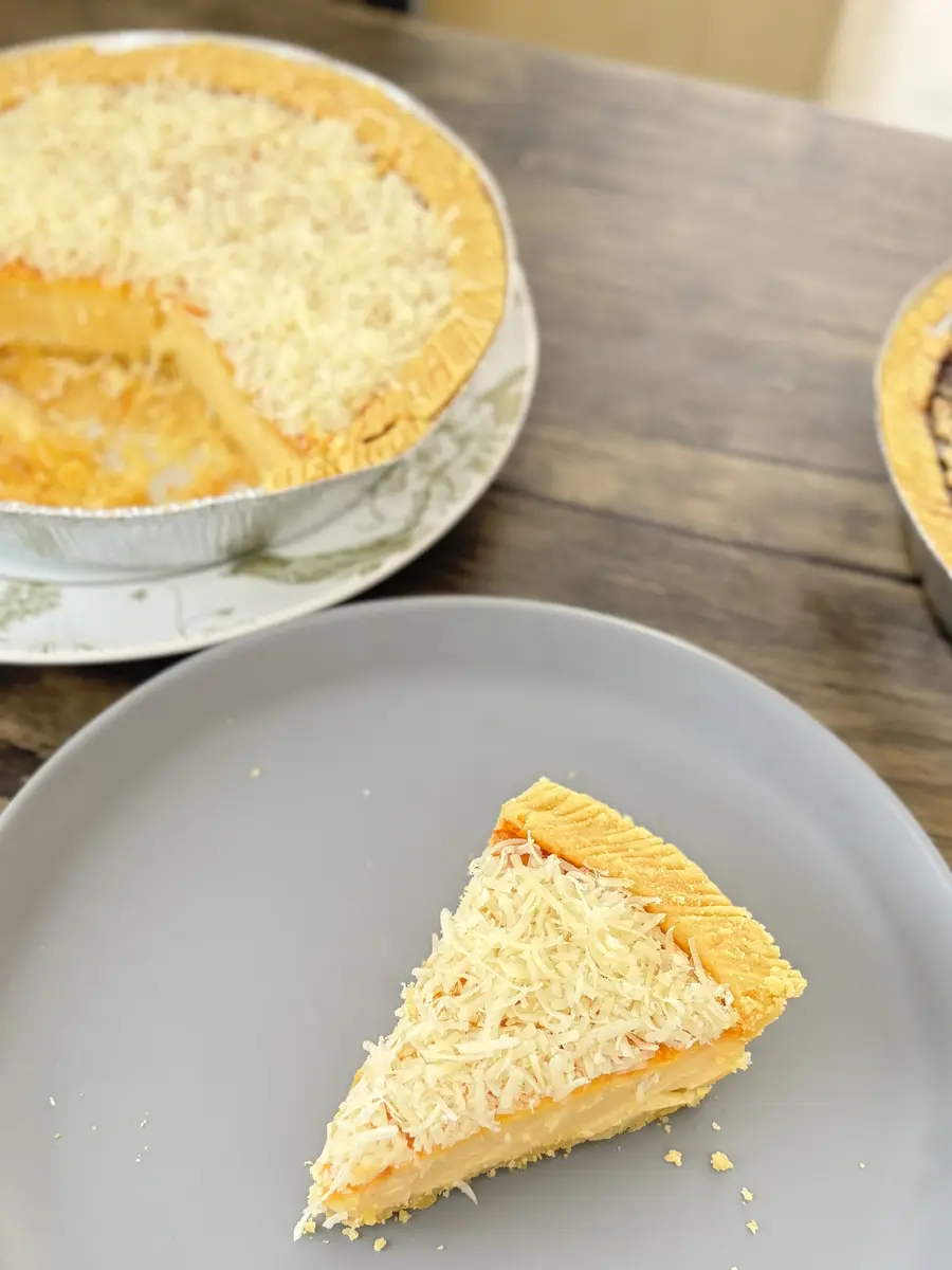 Satu potong Kue Lontar keju di piring, dengan loyangnya yang sudah dipotong di belakang