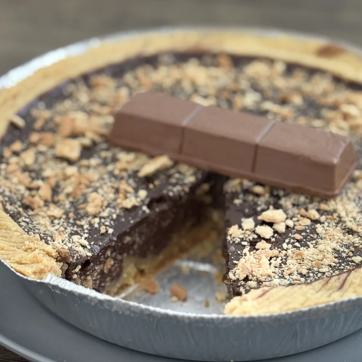 Loyang Kue Lontar cokelat lumer yang sudah dipotong, bertabur remahan biskuit Regal dengan batang cokelat di atasnya