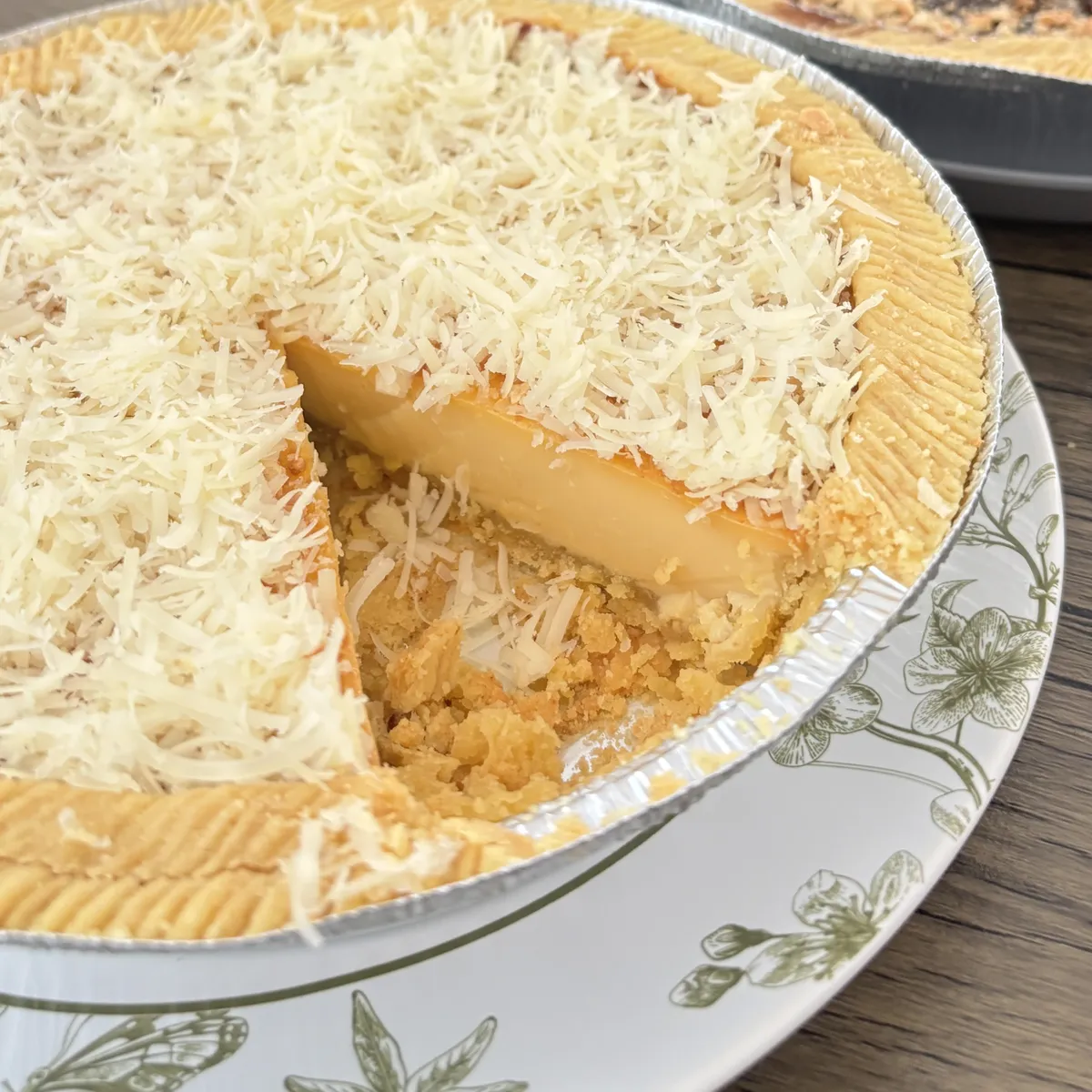 Loyang Kue Lontar keju yang sudah dipotong satu bagian, memperlihatkan lapisan custard lembut di bawah parutan keju cheddar melimpah