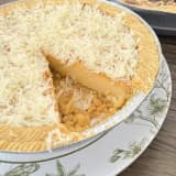 Loyang Kue Lontar keju yang sudah dipotong satu bagian, memperlihatkan lapisan custard lembut di bawah parutan keju cheddar melimpah