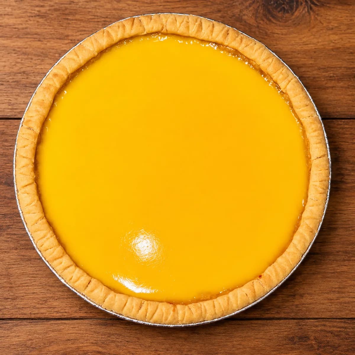 Satu loyang Kue Lontar original dilihat dari atas: custard kuning keemasan dengan pinggiran kulit pie bergerigi dalam loyang aluminium